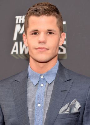 A portrait photo of Max Carver wearing Deep blue Coat and brown blue shirt.